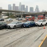 Multiple cars involved in a chain-reaction crash on a Southern California freeway with the Los Angeles skyline in the background, illustrating multi-vehicle collision liability for the middle car.